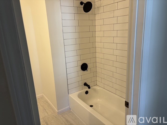 A white tiled bathroom with a white bathtub and a black shower head.