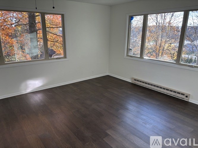 A room with wooden floors and two windows showing autumn trees outside.