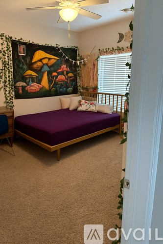 A bedroom with a purple bed and a painting on the wall.