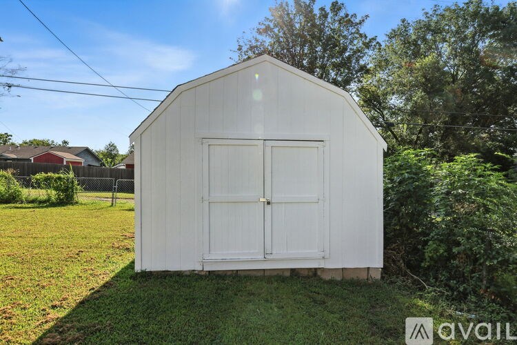A white shed with a glass window is situated in a grassy area.