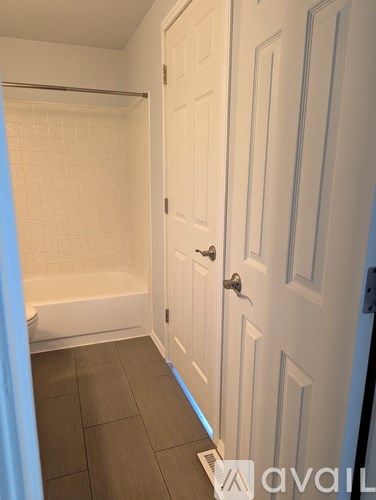A white door is in a bathroom with a white tub and brown tile floor.