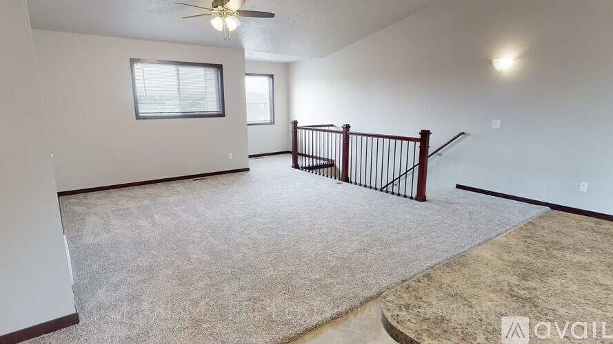 A spacious room with a carpeted floor, a ceiling fan, and a staircase with a railing.