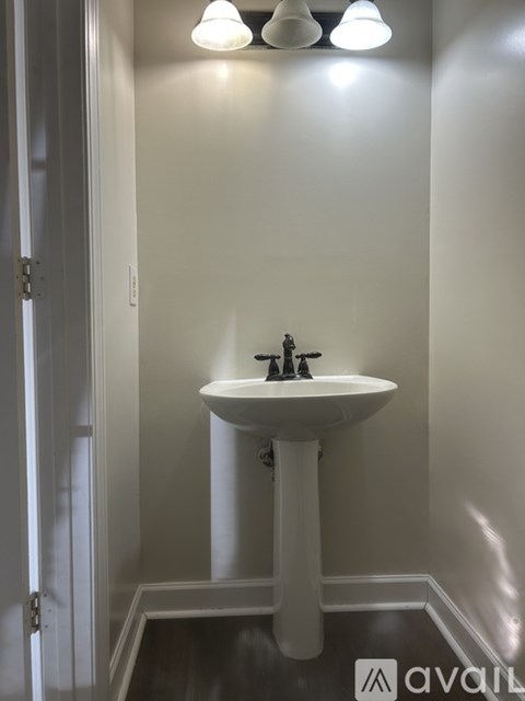 A white pedestal sink with a silver faucet under a light fixture.