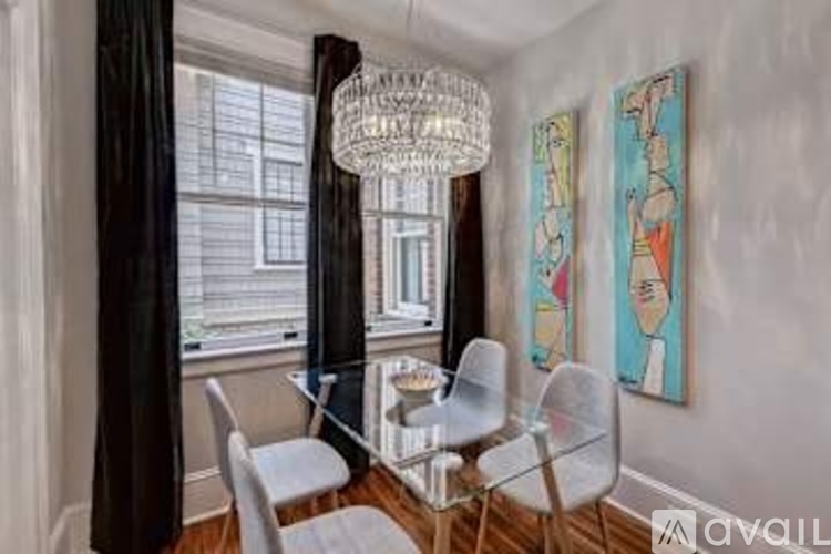 A dining room with a glass table and chairs, a chandelier, and two paintings on the wall.