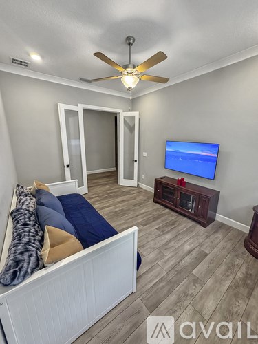 A living room with a white couch and a flat screen TV mounted on the wall.