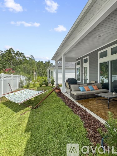 A backyard with a lawn, a hammock, and a patio area.