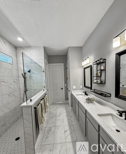 A bathroom with a white tiled floor and walls, a walk-in shower, and a double sink vanity.