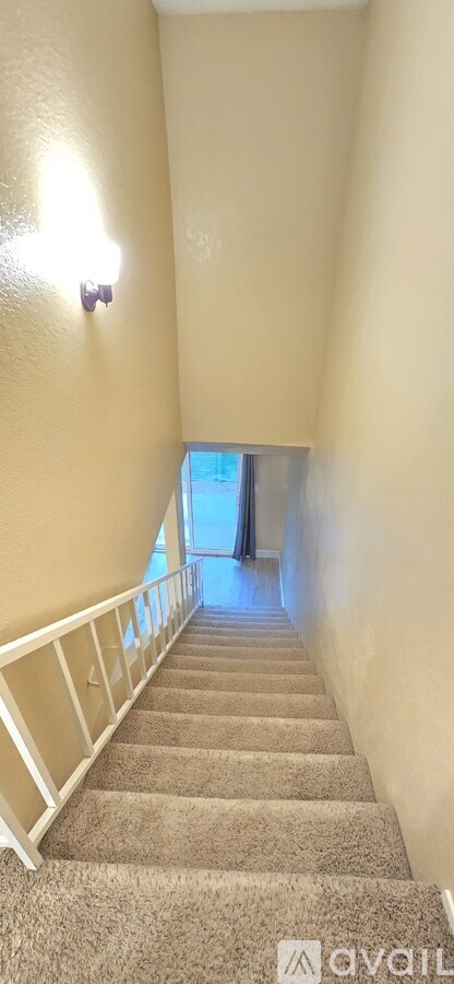 A staircase with beige carpeting and white railings leads to a bright room.