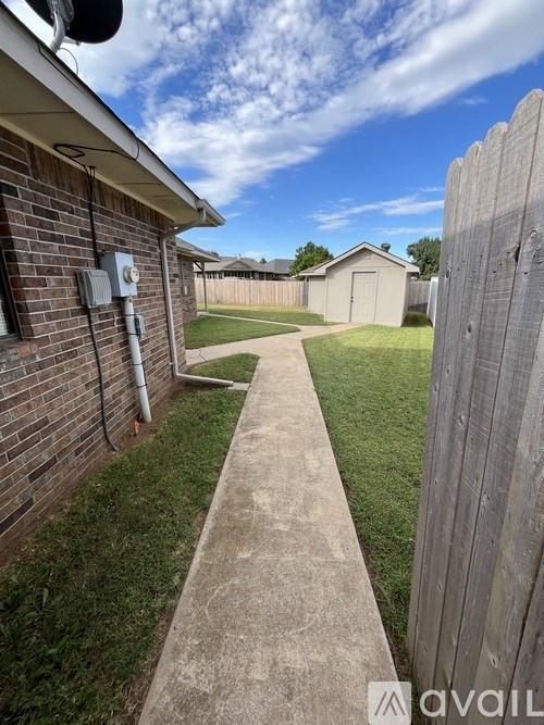 A backyard with a wooden fence and a concrete pathway.