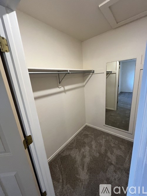 A white door with a gold handle is open to a small, empty room with a grey carpet.