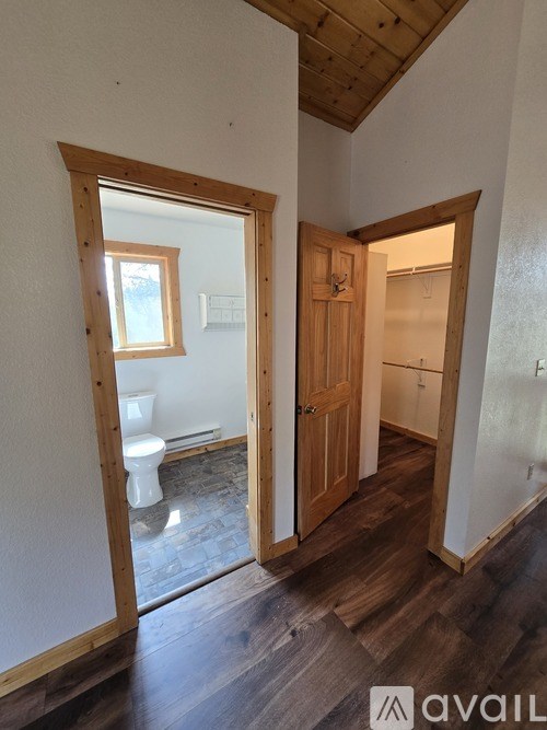 A room with wooden floors and walls, a toilet, and a window.