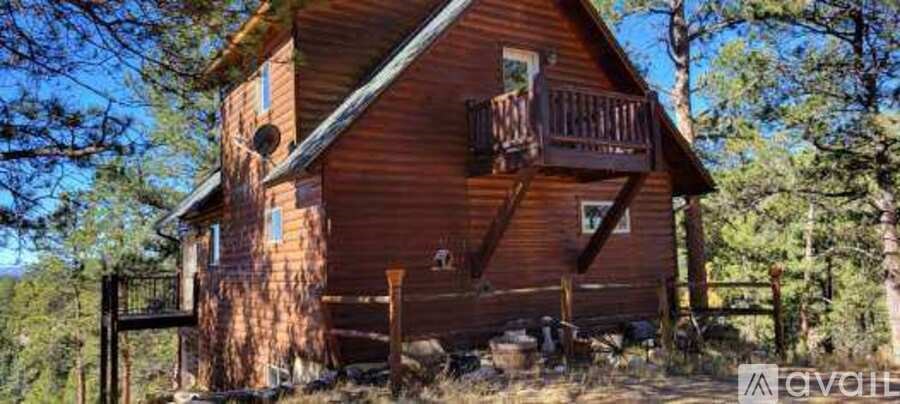 A wooden cabin with a balcony is surrounded by trees.