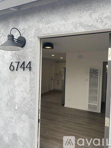 A room with a white door and a lamp on the wall with the number 6744 written on it.