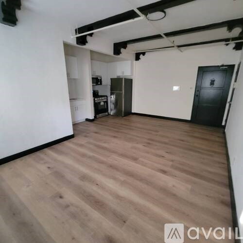A room with wooden flooring and a kitchen area in the background.