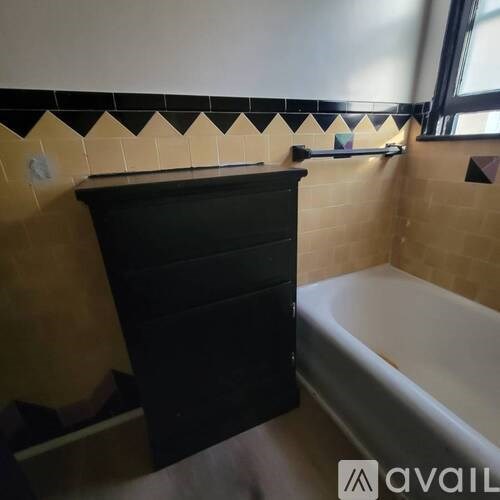 A black dresser sits in a bathroom next to a bathtub.