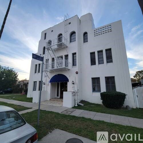 A white building with a blue awning and a car parked in front.