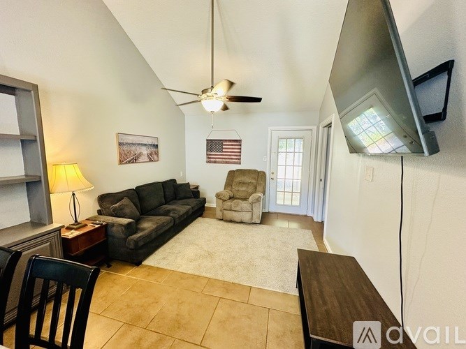 A living room with a grey couch, a brown coffee table, a ceiling fan, and a flat screen TV mounted on the wall.