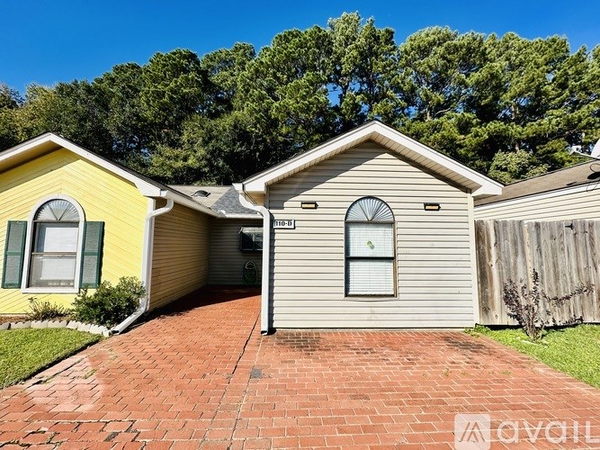 A house with a yellow and a beige exterior is surrounded by a brick walkway and greenery.