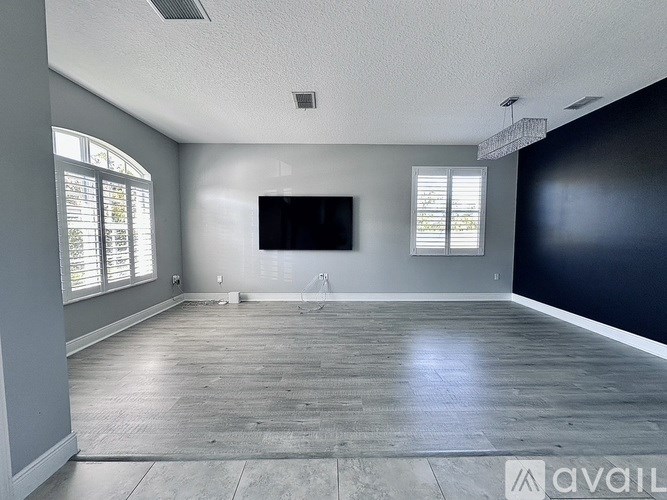 A spacious room with wooden flooring and a large window on the left side.