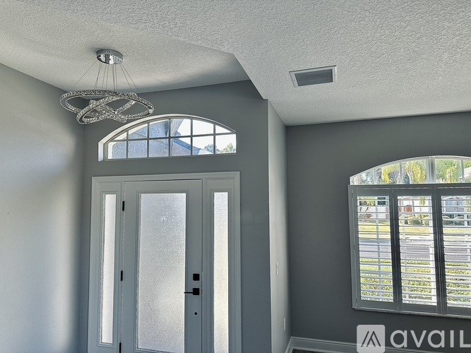 A room with a white ceiling, a chandelier, a window with blinds, and a door with frosted glass.