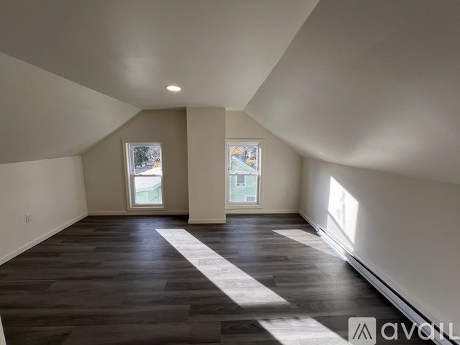 A spacious room with wooden flooring and two windows.