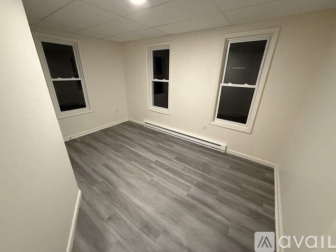 A room with grey flooring and three windows.