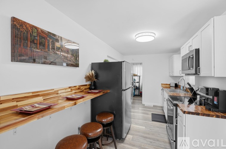 A kitchen with a refrigerator, bar stools, and a painting on the wall.