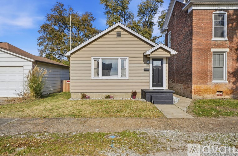 A small house with a grey roof and a brown door is surrounded by a grassy area.