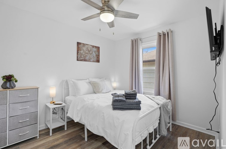 A bedroom with a large bed, a ceiling fan, and a television mounted on the wall.