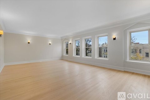 A spacious room with wooden flooring and a row of windows.