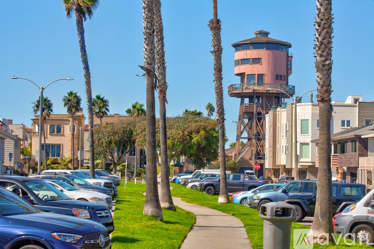 A parking lot with cars and palm trees in front of a pink tower.