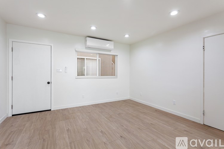 A room with a window, wooden floor, and white walls.