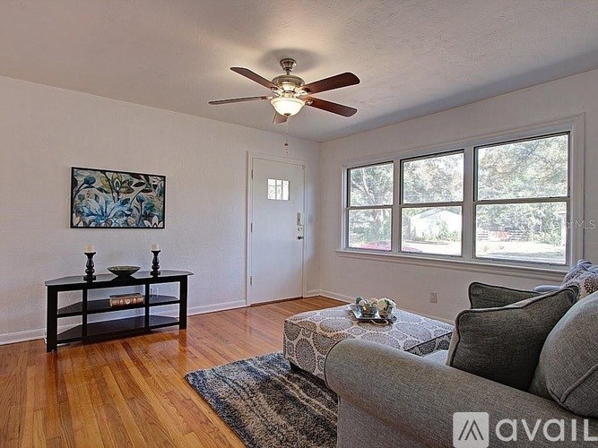 A living room with a grey couch, a coffee table, a painting, a ceiling fan and a rug.