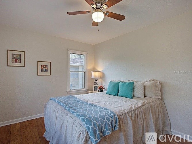 A bedroom with a bed, a ceiling fan, and two pictures on the wall.