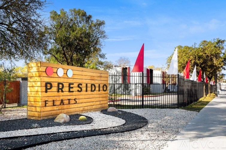 A sign that says "Presidio Flats" is in front of a fence with flags.