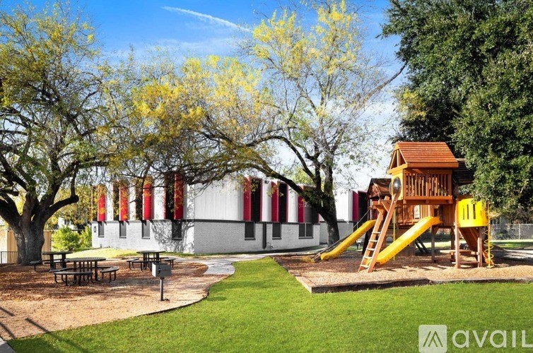 A playground with a yellow slide and picnic tables in front of a building with red and white stripes.