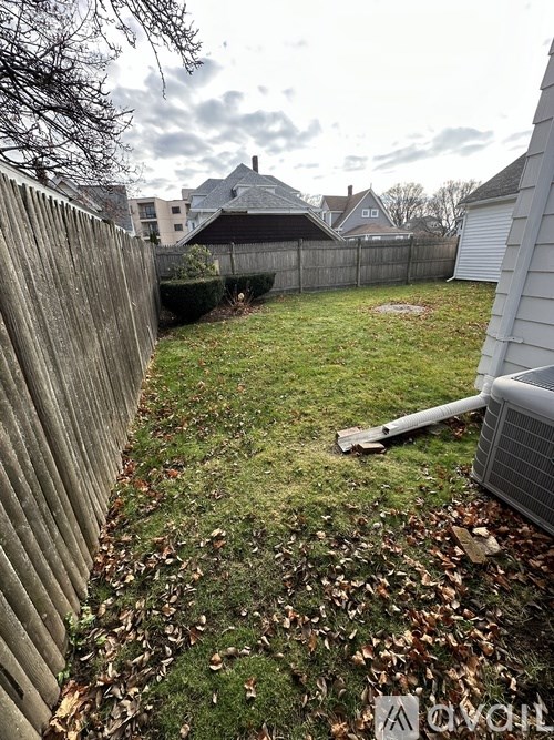 A backyard with a wooden fence and a grassy area with fallen leaves.