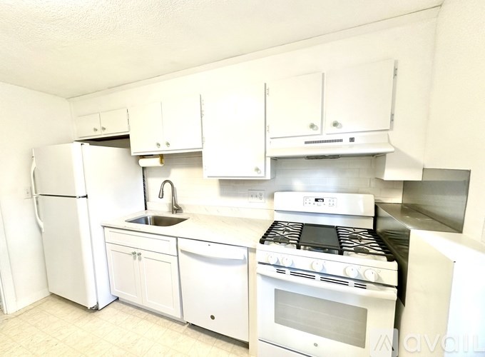 A white kitchen with a stove, sink, and cabinets.