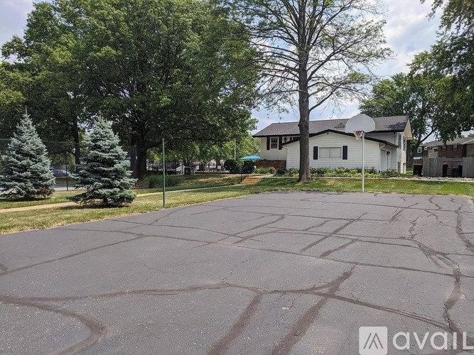A large, empty parking lot with a house and trees in the background.