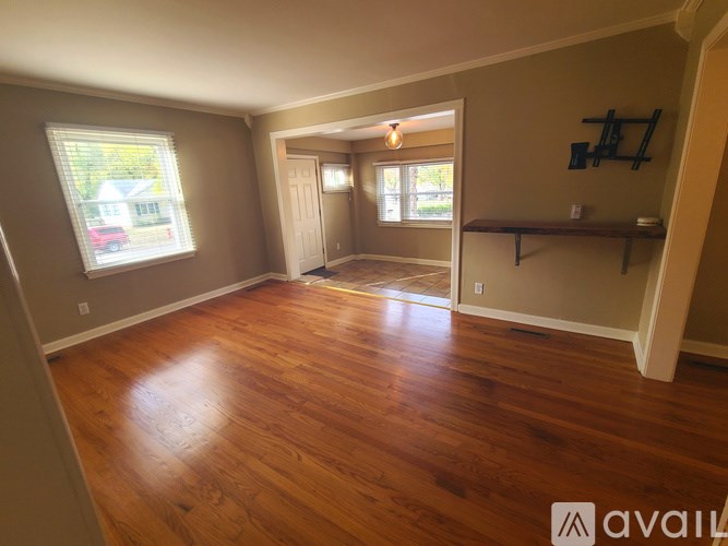 A room with wooden floors and a window showing a red car and a house.