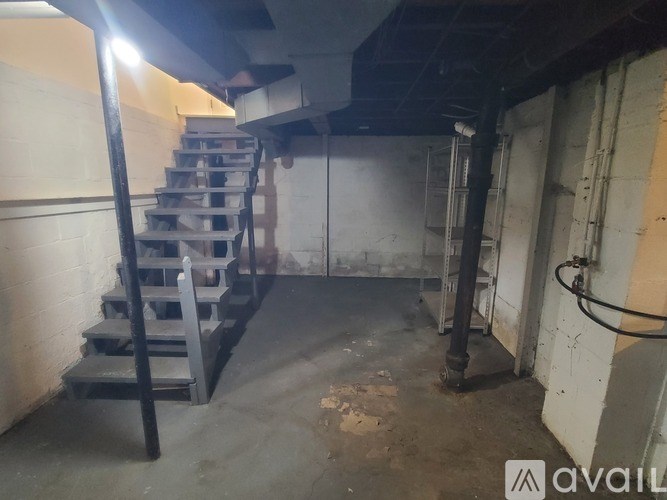 A dimly lit industrial space with a metal staircase and a pipe running along the wall.