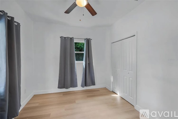 A room with a ceiling fan and a window with curtains.