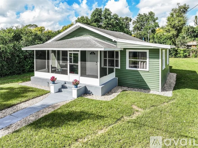 A green house with a porch and a small garden.