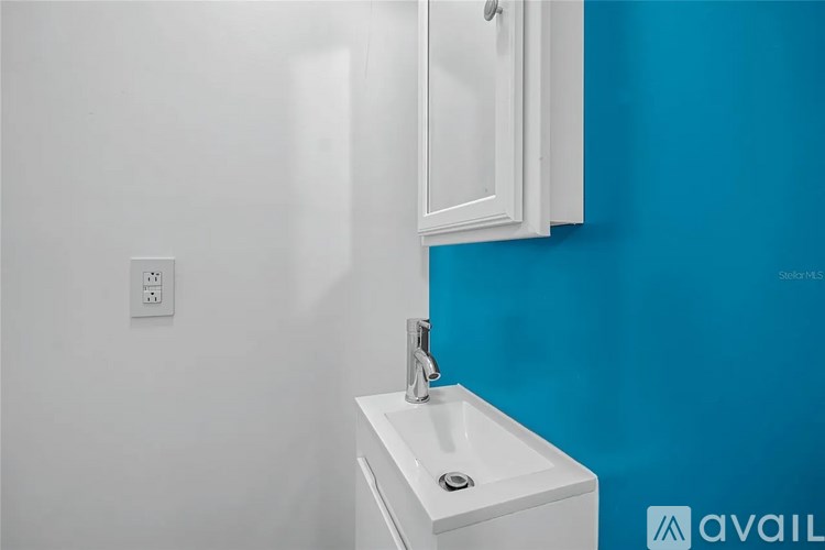 A white sink with a silver faucet is on a white countertop against a blue wall.