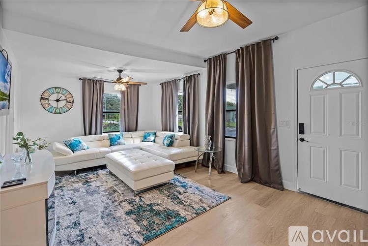 A living room with a white couch, a ceiling fan, and a rug on the floor.