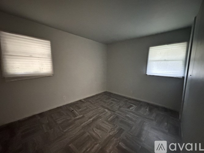 A room with a wooden floor and two windows with blinds.