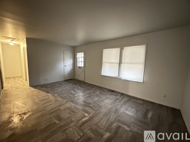 A room with wooden flooring and two windows with blinds.