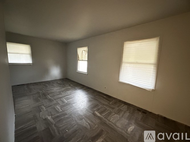 A room with wooden flooring and two windows.