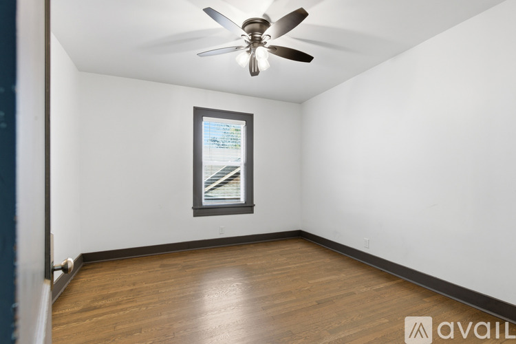 A room with a ceiling fan and a window showing a view of a building.