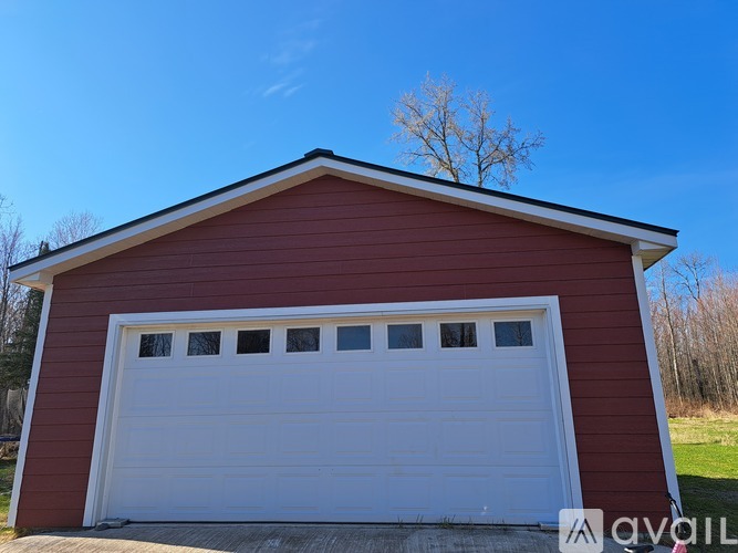 A red garage with a white door is situated in a grassy area.